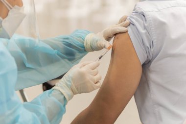 Koruyucu giysili doktor hastaya koronavirüs hastalığı aşısı yapıyor..