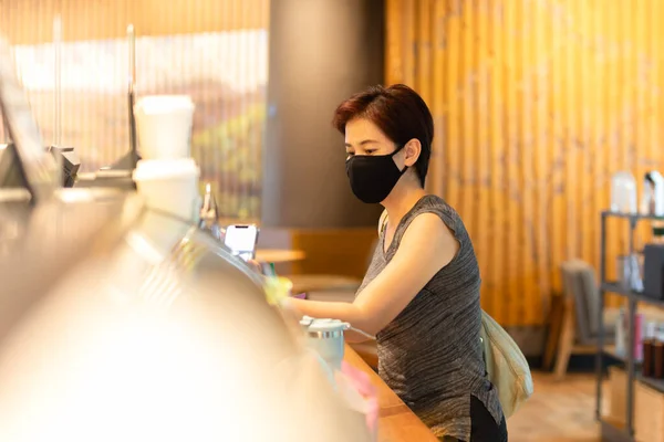Cliente mujer con máscara protectora pagando factura por teléfono celular en cafetería. —  Fotos de Stock
