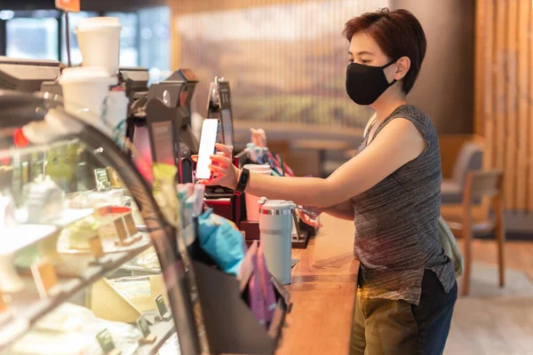 Kobieta klient z maską ochronną płacąc rachunek przez telefon komórkowy w kawiarni. — Zdjęcie stockowe