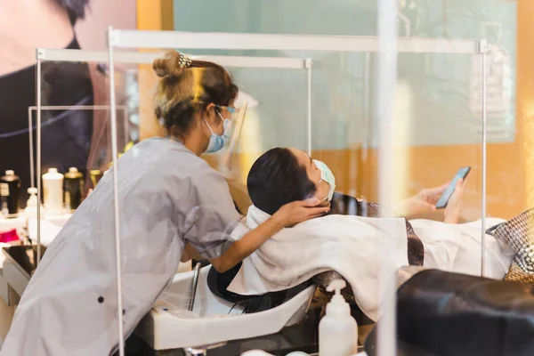 Hairdresser with mask washing the clients hair during Covid-19 pandemic. — Foto de Stock