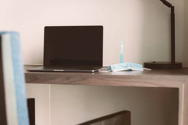 Nueva computadora portátil normal y máscara médica en la mesa en la habitación del hotel. — Foto de Stock