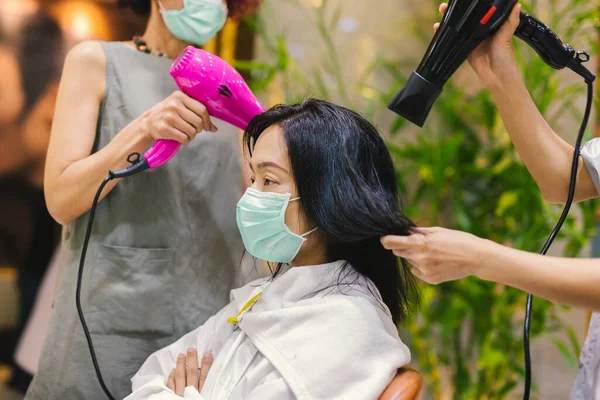 Mujer con máscara médica secándose el pelo en la peluquería. — Foto de Stock