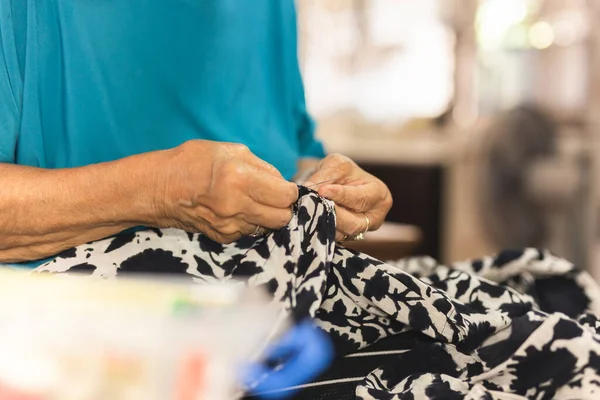 Las manos de la mujer anciana usando aguja e hilo para reparar un vestido. —  Fotos de Stock