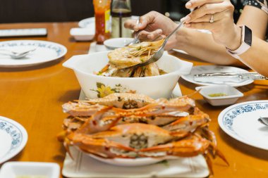 Yemek masasında çatal ve kaşıkla karides tutan Asyalı kadın. İç mekan