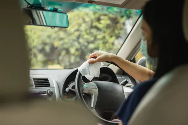 Vrouw schoonmaken stuurwiel met natte veeg in een auto coronavirus pandemie. — Stockfoto