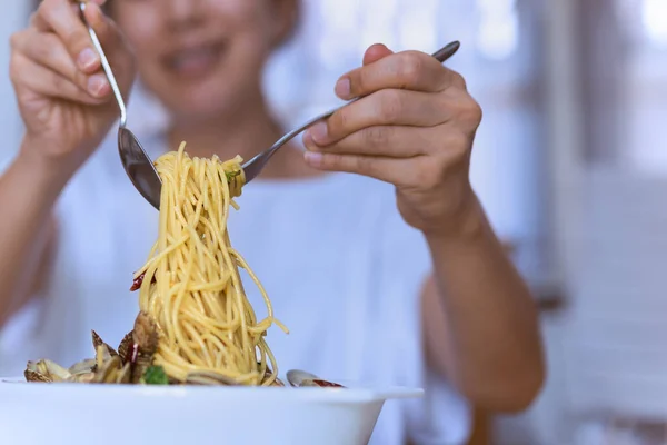 Kvinde spiser velsmagende italiensk spaghetti på hvid skål med ske og gaffel. - Stock-foto