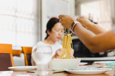 Beyaz kâse üzerinde çatal ve kaşıkla spagetti yiyen kadın..