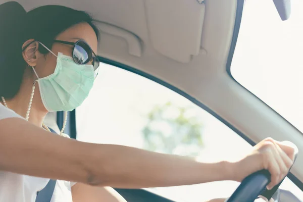 Kobieta prowadząca samochód w masce medycznej i okularach przeciwsłonecznych na twarzy. Ochrona zdrowia i wirusów. — Zdjęcie stockowe
