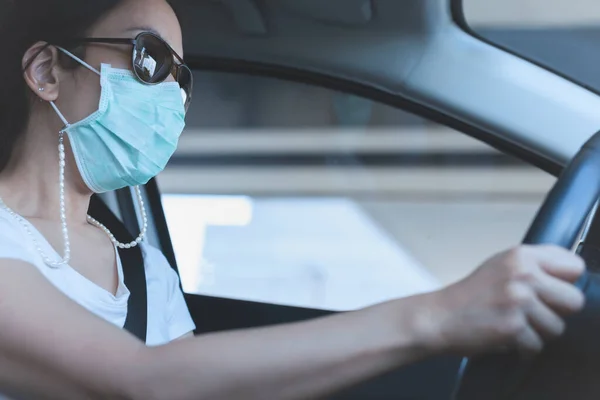 Kobieta prowadząca samochód w masce medycznej i okularach przeciwsłonecznych na twarzy. Ochrona zdrowia i wirusów. — Zdjęcie stockowe