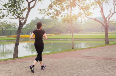 Genç Asyalı kadın sabahın erken saatlerinde şehir parkında koşuyor..