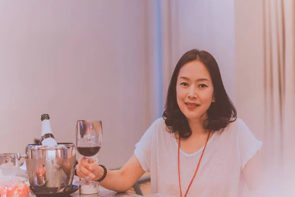 Boldog mosolygós ázsiai nő kezében szemüveg piros vacsoraasztalnál otthon. — Stock Fotó
