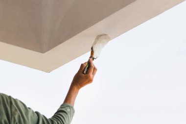 Bir kişinin dış tavan kenarını fırçayla boyaması.