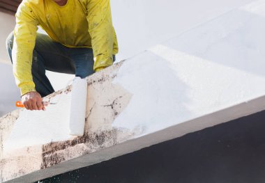 Bir ressam, dış duvara silindirle taze beyaz boya sürüyor.