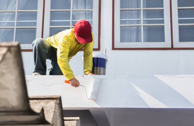 Bir ressam, dış duvara silindirle taze beyaz boya sürüyor.