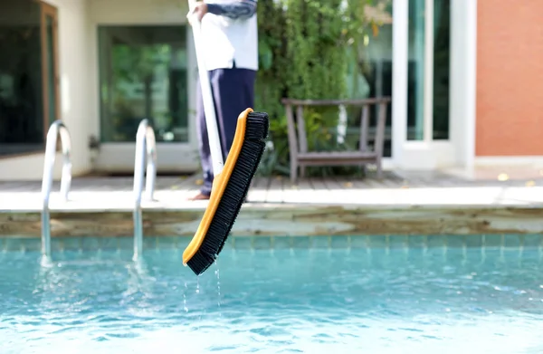 Mna is cleaning a swimming pool with a brush