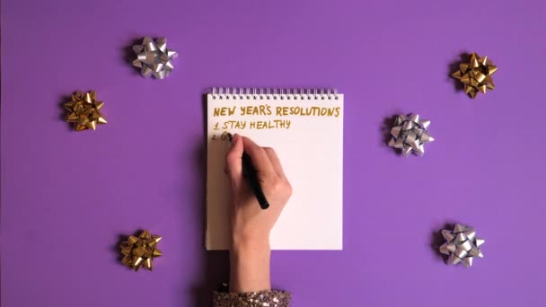 Ženy rukou psaní nové roky usnesení v učebnici na fialovém pozadí. — Stock video