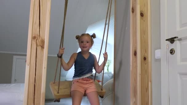 Glückliches blondes Mädchen mit Sommersprossen und Zöpfen reitet zu Hause auf einer Holzschaukel — Stockvideo