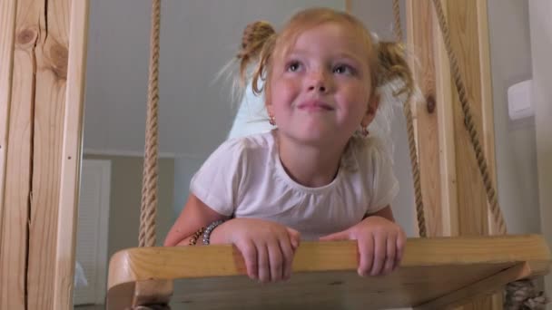 Menina loira com sardas passeios no balanço de madeira e sorri para a câmera — Vídeo de Stock