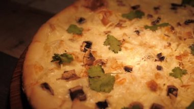 Peynirli, mantarlı ve otlu lezzetli bir pizza. Kamera pizzanın yan tarafında daireler çiziyor. Kavram: Menünün sunumu.