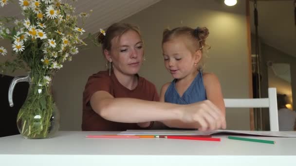 母と娘はスケッチブックで一緒に絵を描き テーブルに座っている色鉛筆で家に座っています 隣には大きな花瓶の花が立っている ホームスクーリングと隔離 — ストック動画