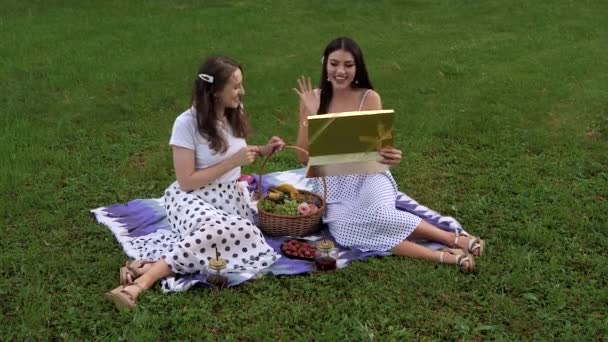 Deux jolies filles en robes légères échangent des cadeaux pour le 14 février sur une pelouse verte. — Video
