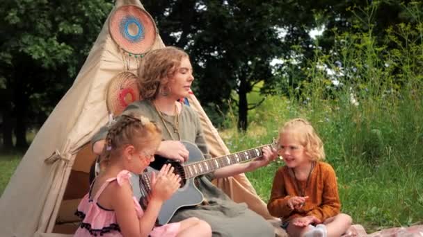 Семья Бохо. Мама играет на гитаре с двумя дочерьми в природе. — стоковое видео
