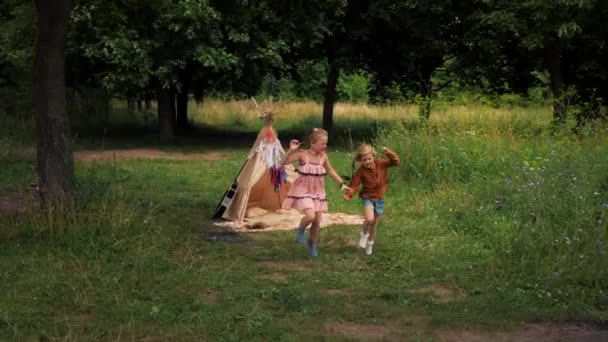 Dos chicas hippies cogidas de la mano y corriendo juntas sobre hierba verde. — Vídeo de stock
