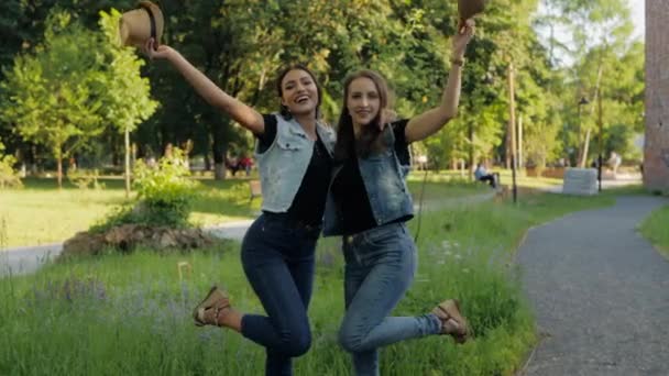 Two girlfriends throw their hats up, having fun outdoors in summer. — Stock Video