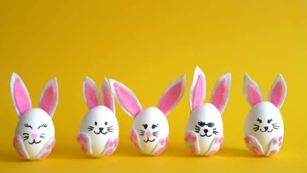 Roliga påskägg dekorerade som kaniner byta plats på den gula bakgrunden. — Stockvideo