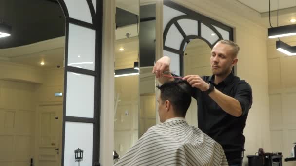 Barber membuat potongan rambut untuk kliennya. Di dalam ruangan di toko cukur. — Stok Video
