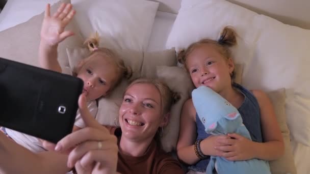 어머니는 태블릿으로 비디오 메시지를 금발인 침대에 스마트폰 카메라로 마스를 만든다 — 비디오