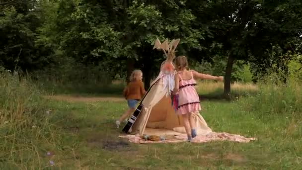 Dos chicos hippies jugando al aire libre. Boho niñas corriendo alrededor de la wigwam. — Vídeo de stock