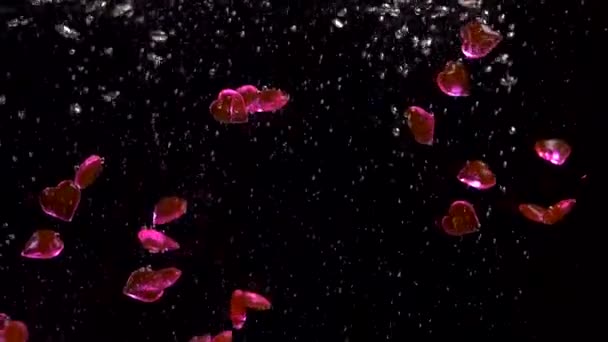 Pink glass hearts fall in water forming oxygen bubbles. Valentines day concept. — Stockvideo