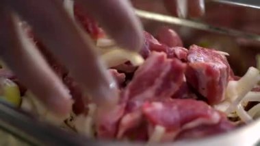 Eldivenli şef çiğ etle soğanı karıştırıyor..