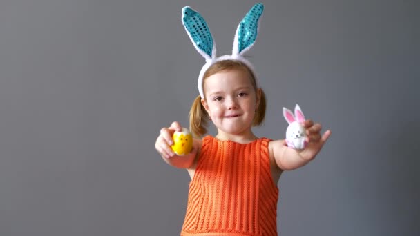 Funny cute European girl shows painted Easter eggs. Gray wall background. — Stock Video