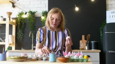 Sarışın kız mutfakta paskalya yumurtası süslüyor. Kutsal Paskalya Pazarı. Kadın fırçayla yumurta boyuyor.. 