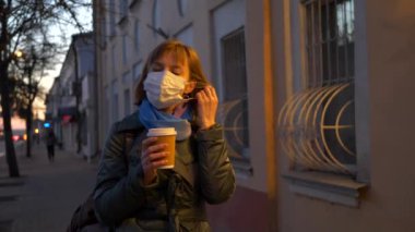 Cam kahveli bir kızın şehir portresi. Kadın antiviral maskesini çıkarıp dışarıda sıcak bir şeyler içiyor.