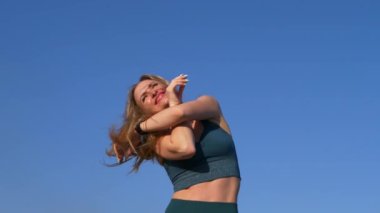 Mavi gökyüzünün önünde rüzgarda dalgalanan uzun saçlı güzel sarışın kadının portresi. Kız spor tişörtü giyiyor.