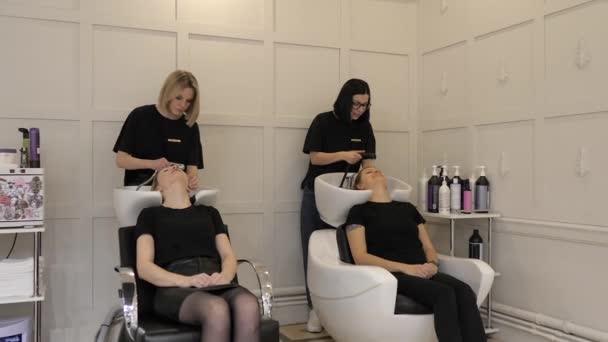 Σαλούν ομορφιάς. Δύο κομμώτριες πλένουν κεφάλια γυναικών πελατών. — Αρχείο Βίντεο