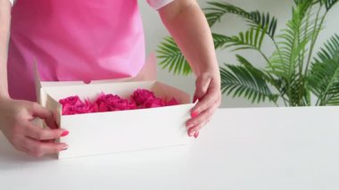 Pembe önlüklü kız içinde pembe kekler olan bir kutu hazırlıyor. Kadın eller doğum için beyaz bir kutuda tatlı paketliyorlar. Konsept: Yemek teslimatı.