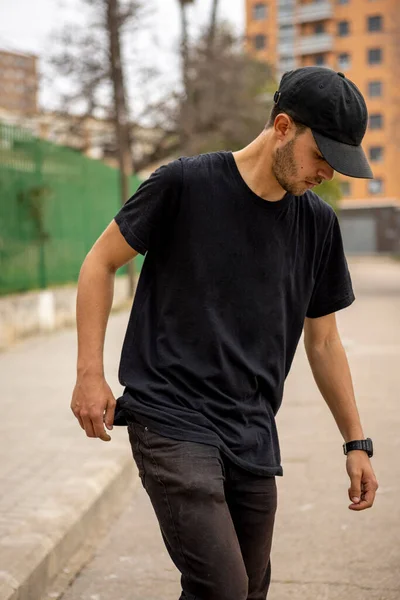 Joven hombre caucásico de Italia con una camisa negra y gorra caminando por la calle — Foto de Stock