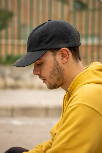 Retrato de un joven varón con capucha amarilla y gorra negra en una calle — Foto de Stock