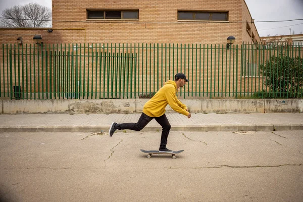 A young male skateboarding on the street in a yellow hoodie and a black cap — Stock Photo, Image