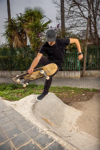 Young caucasian male in a black shirt and cap jumping with his skateboard — Stock Photo, Image