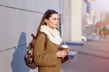 Güzel esmer kadın sokakta duran, sıcak çay veya kahve bir çanta ve fincan tutan