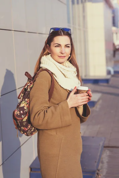 Wanita berambut cokelat cantik memegang tas dan secangkir teh panas atau kopi, berdiri di jalan — Stok Foto