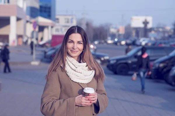 Bella donna bruna in possesso di una borsa e una tazza di tè caldo o caffè, in piedi in strada — Foto Stock