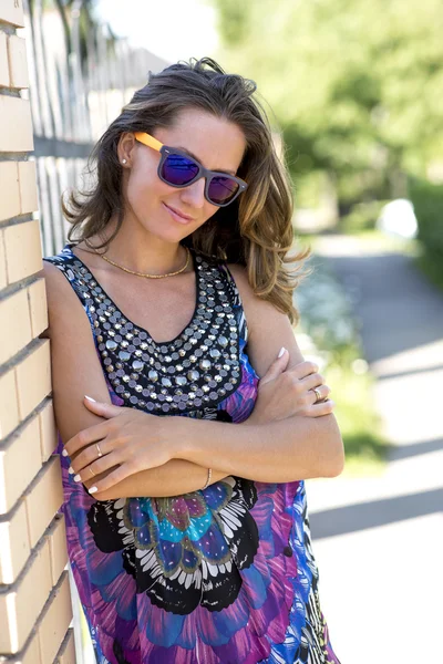 Hermosa mujer de pie cerca de la pared de ladrillo en gafas, feliz, moda, día soleado brillante . — Foto de Stock