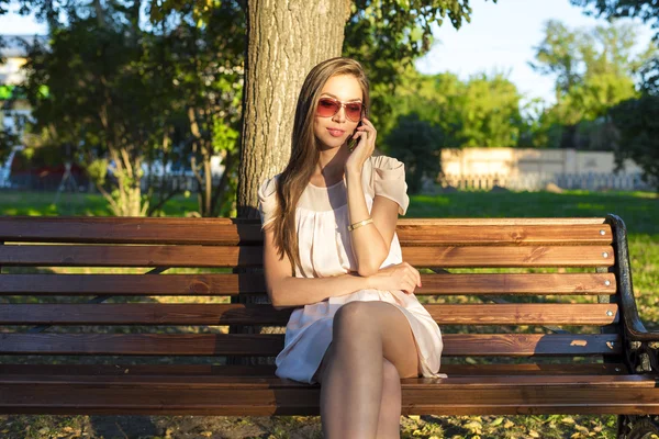 Hermosa chica morena emocional riendo teléfono parque gafas de verano vestido rosa, disfrutar de sus vacaciones en la ciudad — Foto de Stock