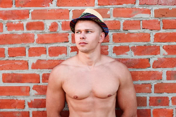 Bodybuilder mit Hut steht an der Wand und blickt in die Ferne — Stockfoto